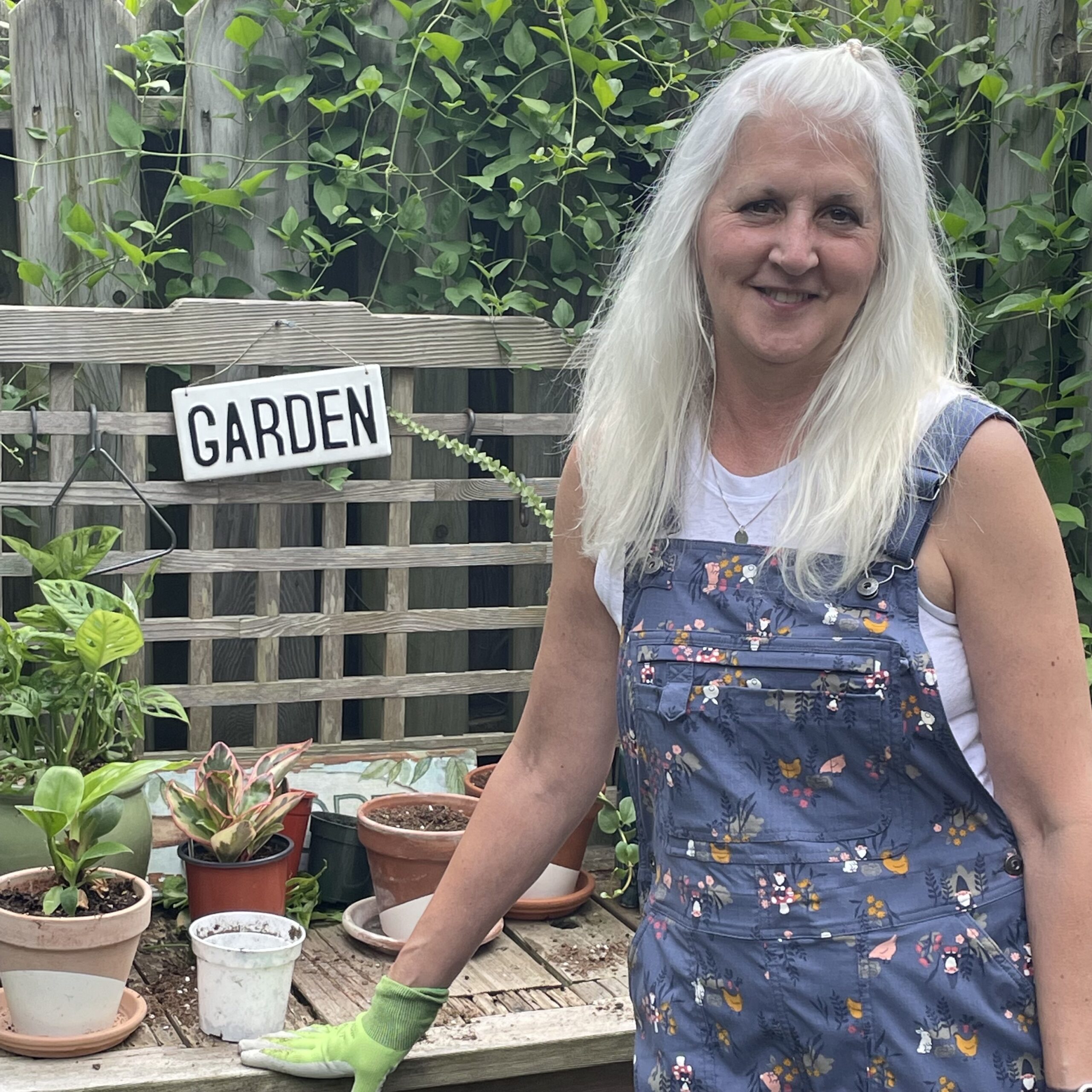 woman in blue overalls standing in front of garden bench
