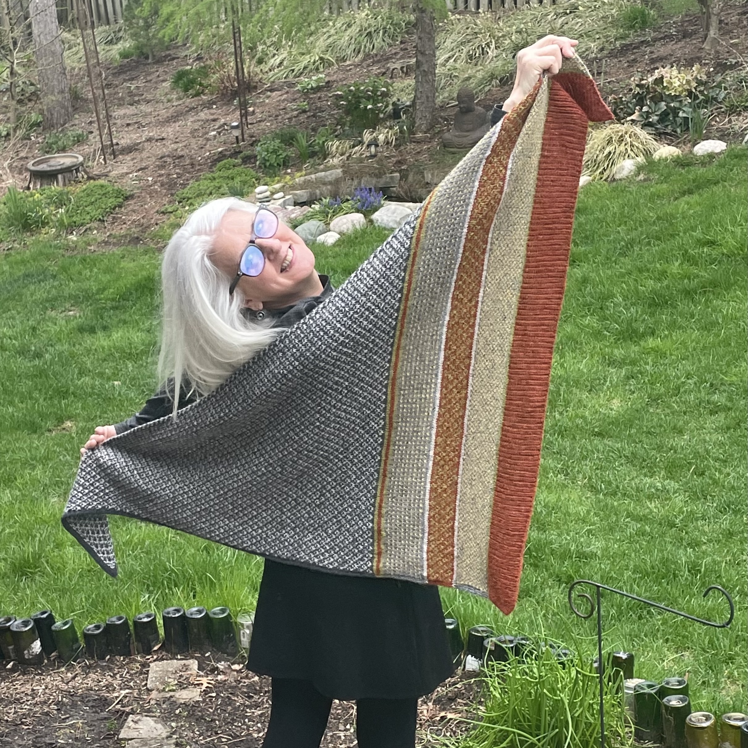 square photo of woman holding up a colorful hand knit shawl
