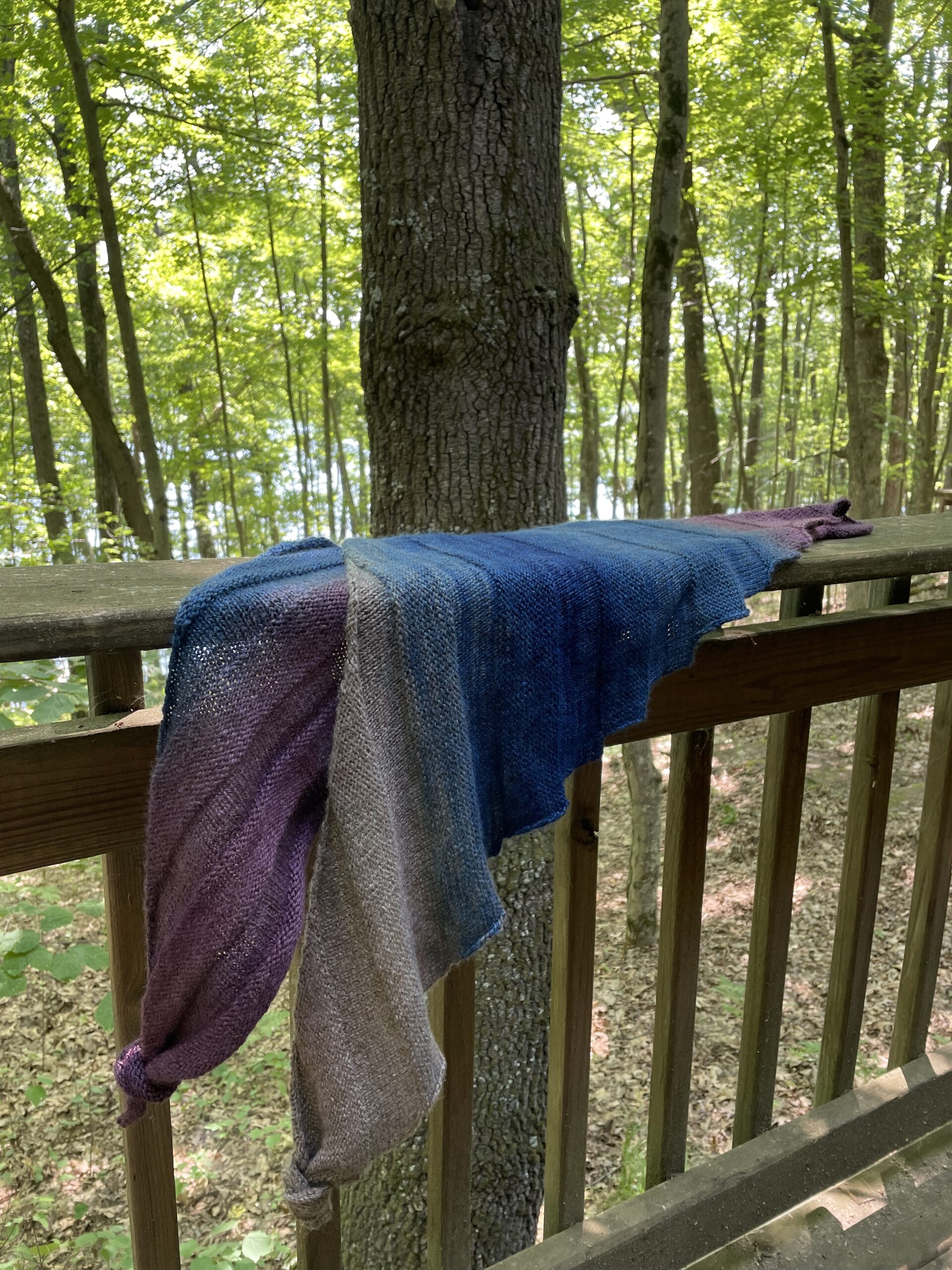 folded knit shawl hanging on deck railing in woods