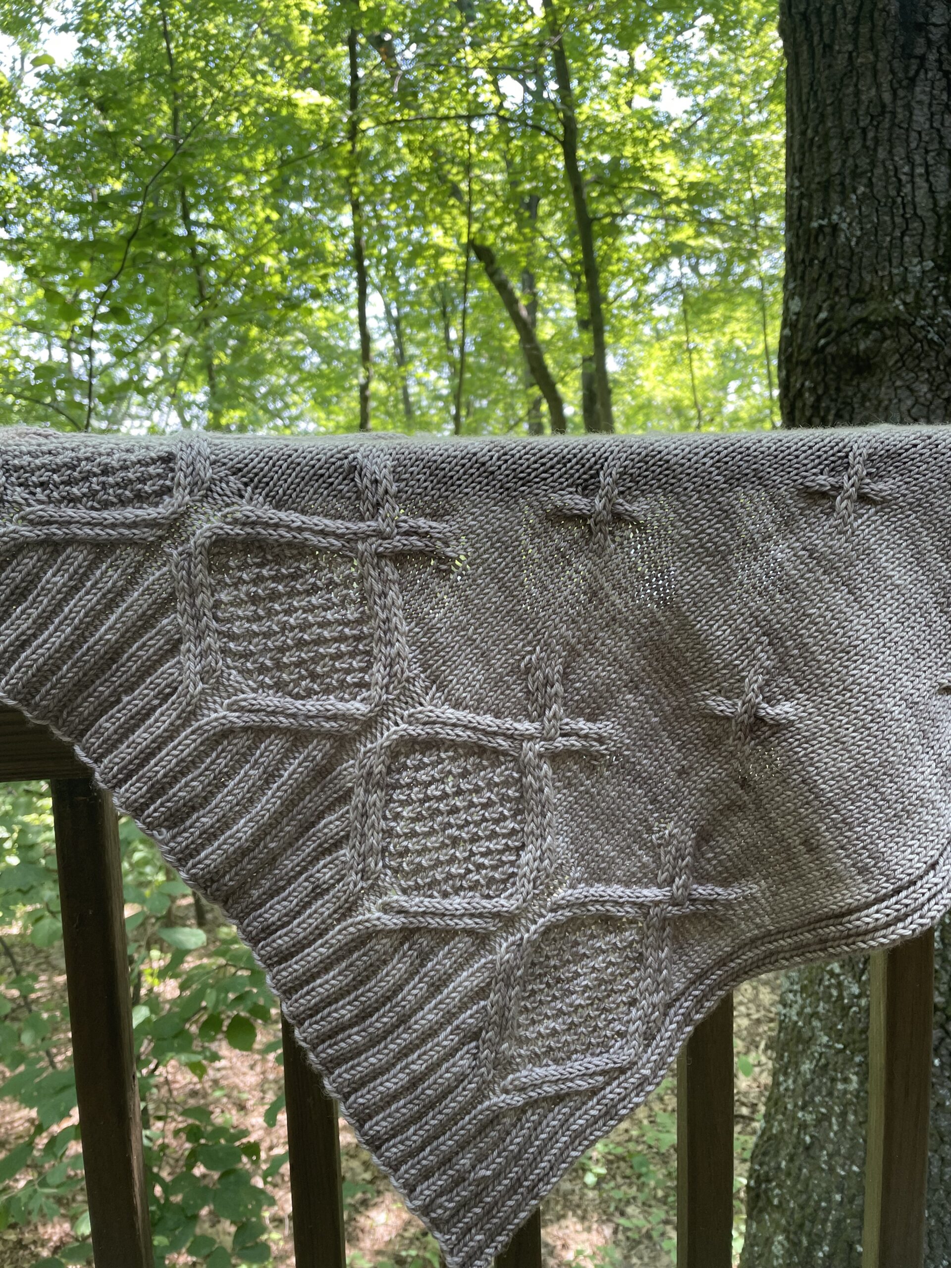 hand knit cable shawl hanging on patio rail